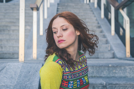 Beautiful redhead girl with long hair and blue eyes posing in an urban context