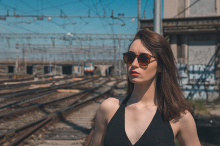 Beautiful young brunette with long hair posing along railroad tracks