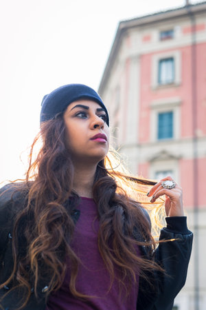 Beautiful Middle Eastern girl with long hair posing in an urban context. Backlight.