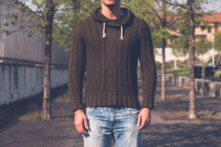 Detail of a young man in jeans and sweater posing in an urban contextの写真素材