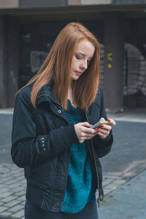 Beautiful young redhead girl texting in the city streetsの写真素材
