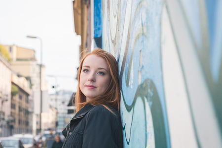 Beautiful young redhead girl posing in the city streetsの写真素材