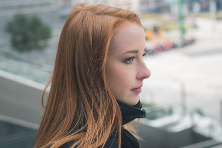 Portrait of a beautiful young redhead girl posing in the city streets