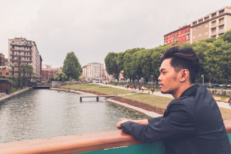 Young handsome Asian model dressed in black posing by an urban artificial basinの写真素材