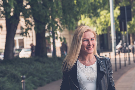 Beautiful blonde girl with white minidress and leather jacket posing in the city streets