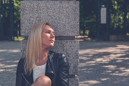 Beautiful blonde girl with white minidress and leather jacket posing in the city streetsの写真素材