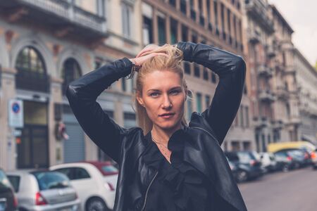Beautiful blonde girl with black minidress and leather jacket posing in the city streetsの写真素材