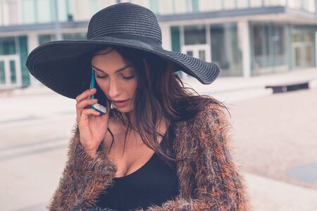 Gorgeous young brunette in black dress talking on phone in an urban contextの写真素材
