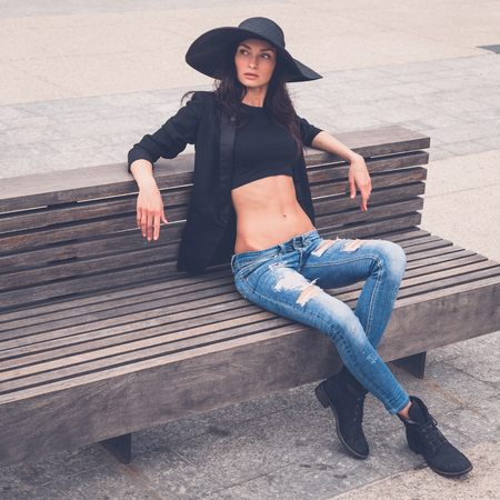 Gorgeous young brunette with hat posing on a benchの写真素材