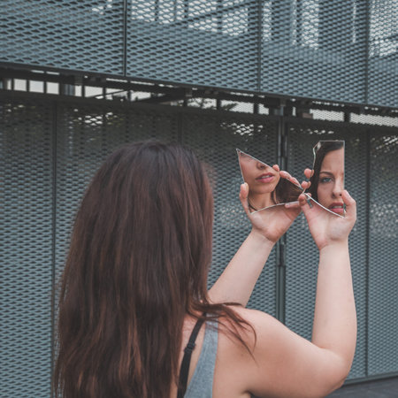 Beautiful young girl in tank top looking at herself in a broken mirror