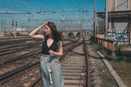 Beautiful young brunette with long hair posing along railroad tracksの写真素材