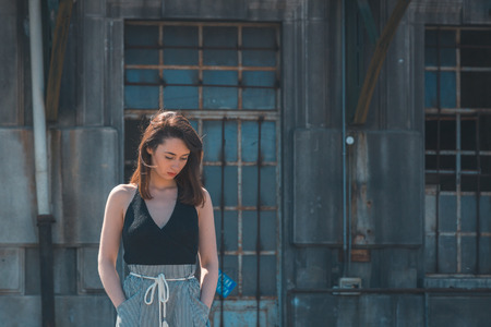 Beautiful young brunette with long hair posing in an industrial areaの写真素材