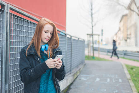 Beautiful young redhead girl texting in the city streetsの写真素材