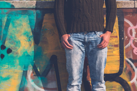 Detail of a young man in jeans and sweater posing in an urban context