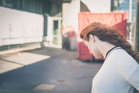 Beautiful redhead girl with long hair and blue eyes posing in an urban contextの写真素材