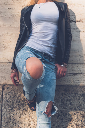 Detail of a beautiful girl wearing ripped jeans and leather jacket posing in the city streetsの写真素材
