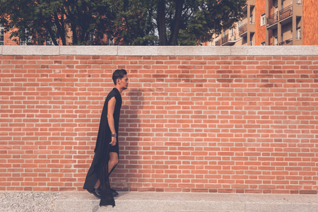 Young handsome Asian model dressed in black tunic posing with a brick wall in backgroundの写真素材