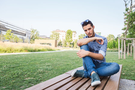 Young handsome man with short hair sitting on a bench in a city parkの写真素材