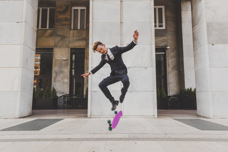 Young handsome Asian model dressed in dark suit and tie jumping with his skateboard
