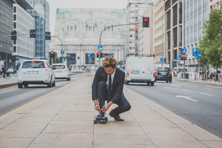 Young handsome Asian model dressed in dark suit and tie posing on his skateboardの写真素材