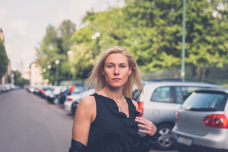 Beautiful blonde girl with black minidress and leather jacket posing in the city streetsの写真素材