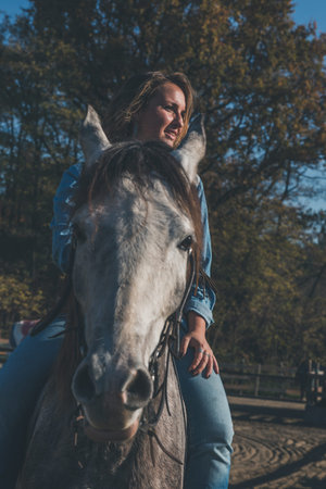Pretty blonde girl riding her grey horse in the countrysideの写真素材