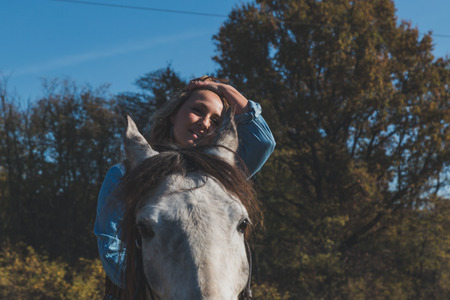 Pretty blonde girl riding her grey horse in the countrysideの写真素材