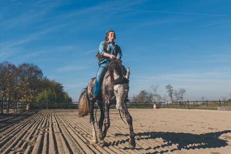 Pretty blonde girl riding her grey horse in the countrysideの写真素材