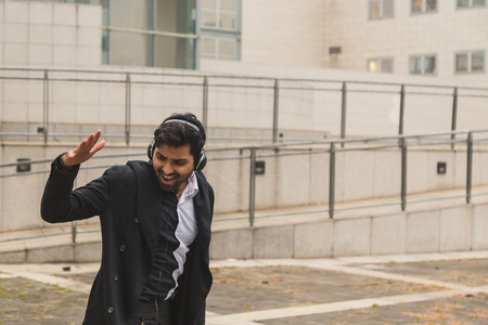 Portrait of a young handsome Indian man with headphones listening to music in an urban contextの写真素材