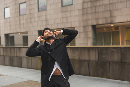 Portrait of a young handsome Indian man with headphones listening to music in an urban contextの写真素材