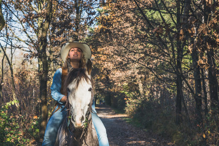 Pretty blonde girl riding her grey horse in the countryside