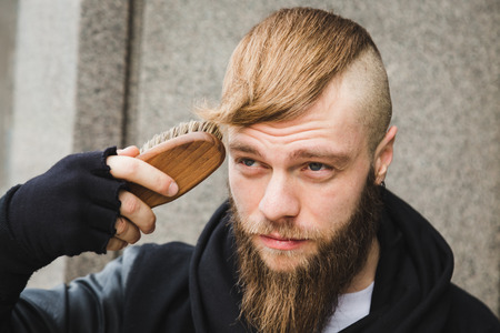 Portrait of a stylish young bearded man brushing his hairの写真素材