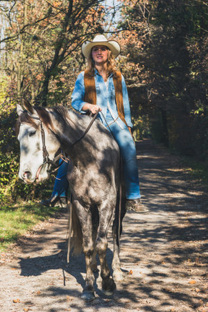 Pretty blonde girl riding her grey horse in the countryside