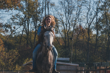 Pretty blonde girl riding her grey horse in the countrysideの写真素材