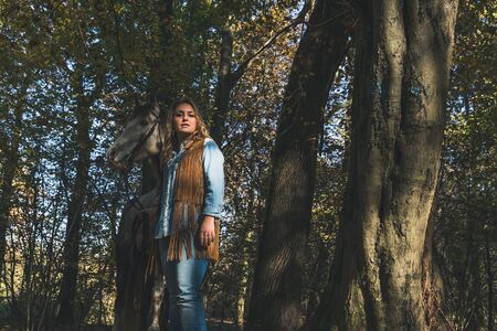 Pretty blonde girl standing by her grey horse in the countrysideの写真素材