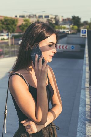 Young beautiful woman with long hair talking on phone in an urban contextの写真素材