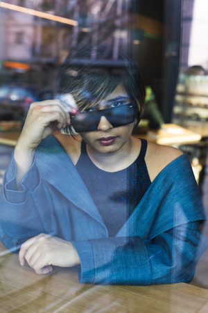 Portrait of a beautiful Indian woman posing behind a reflecting glass. Street fashion and style.の写真素材
