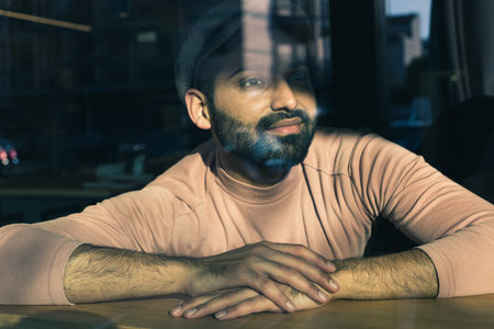 Portrait of a handsome Indian man posing behind a reflecting glass. Street fashion and style.