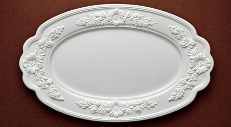 An ornate white oval serving platter with floral embossed detailing rests on a textured brown surfaceの素材