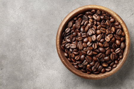 Roasted coffee beans fill a wooden bowl, set on a textured, gray surfaceの素材