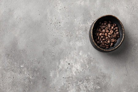 A dark bowl of roasted coffee beans sits on a mottled gray surface, minimal compositionの素材