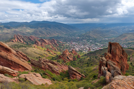 Vast vista reveals a valley town amidst vibrant red rock formations under a cloudy skyの素材