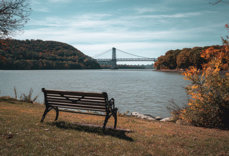Scenic waterscape featuring a bench, a bridge spanning a body of water, and autumnal foliageの素材