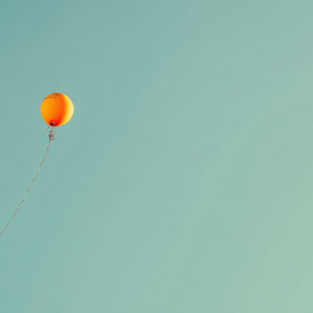 An orange balloon floats tethered against a vast turquoise sky. Minimalist and whimsical sceneの素材