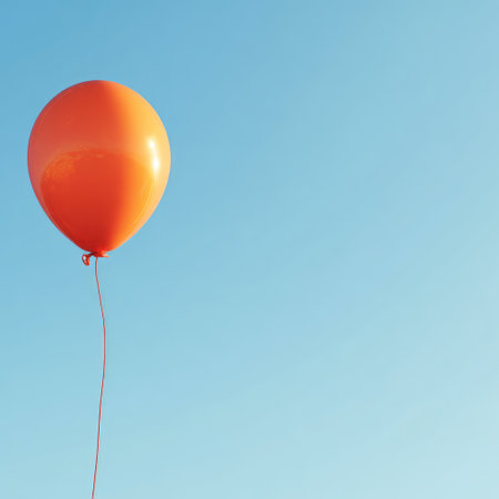 An orange balloon floats alone against a bright blue, cloudless sky, with space for textの素材