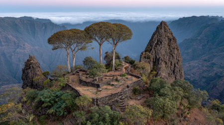 The image captures a scenic vista of a rock formation crowned with trees, set against a backdrop of distant mountains. The composition features a mix of textures and colors, from the rough stone to the greenery and the soft hues of the sky. This scene could be suitable for various commercial or editorial applications.の素材