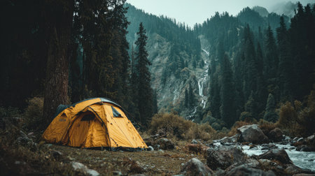 An outdoor scene features a vibrant yellow tent pitched near a river and towering trees. The composition highlights a landscape dominated by lush green foliage and rocky terrain. The image conveys a sense of adventure and nature. Suitable for various editorial and commercial applications.の素材