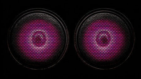 Two circular speaker grills are positioned in a symmetrical arrangement against a dark background. The internal illumination is a vibrant pink, creating a strong contrast. The composition highlights the geometric shapes and textures, and it may be used for various design, technology, or sound-related projects.の素材
