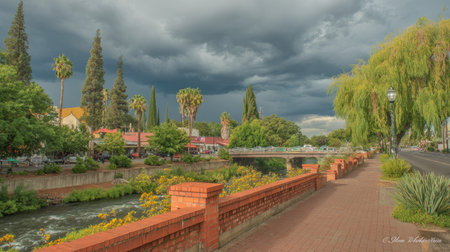 A landscape showcases a river with lush greenery and tall trees under a dramatic, overcast sky. The image features a pathway and a brick wall. The color palette includes shades of green and brown. This image could be used for various purposes, including travel, nature, or environmental themes.の素材