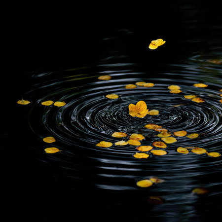 Yellow flower petals rest on dark water surfaces forming concentric ripple patterns. The composition features high contrast with dramatic lighting. This serene image evokes a sense of calm and could be used in design or editorial projects. The dark background adds depth to the scene.の素材